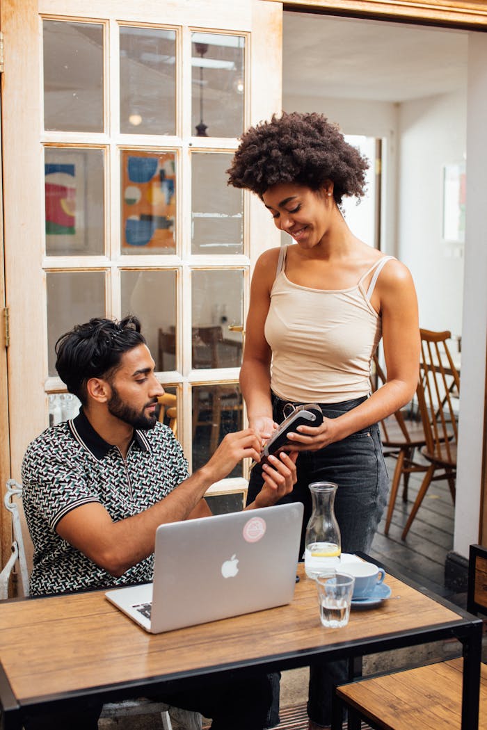 About Man and woman in a café completing a wireless payment using a card reader and laptop.