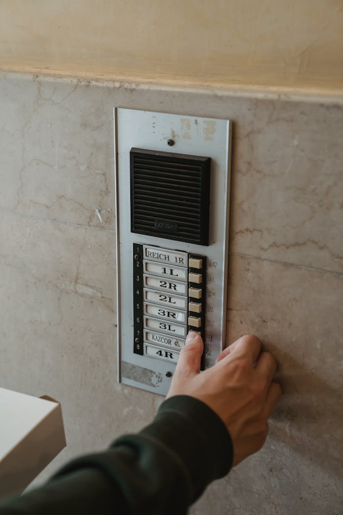 Services Close-up of a hand pressing an intercom button outdoors on a building wall.